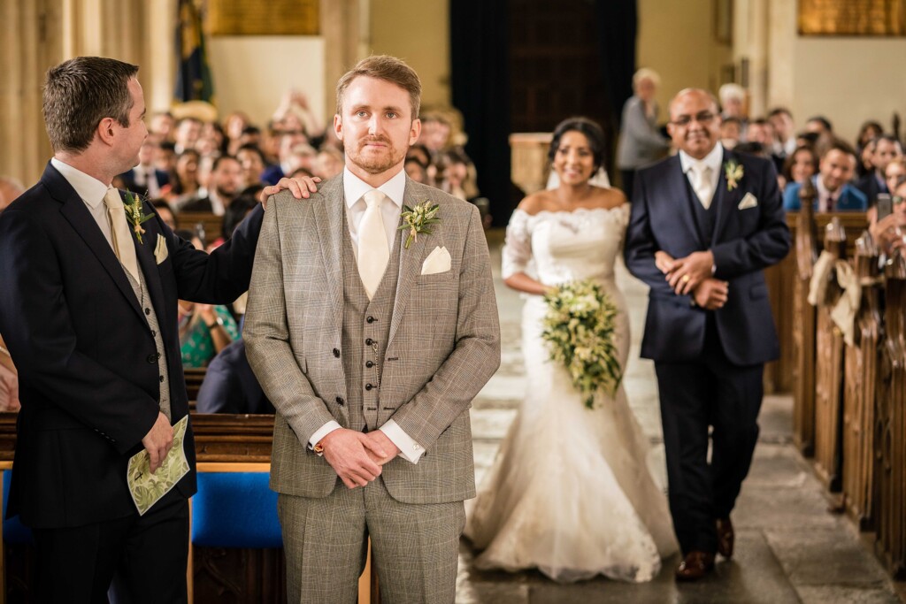 A groom waiting at the front of the church as the bride walks up the aisle