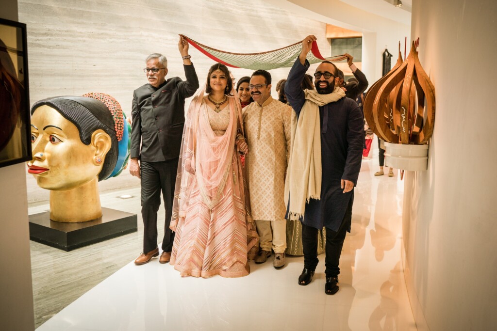 A bride in a pink lehenga walking under a cloth canopy held up by the men around her
